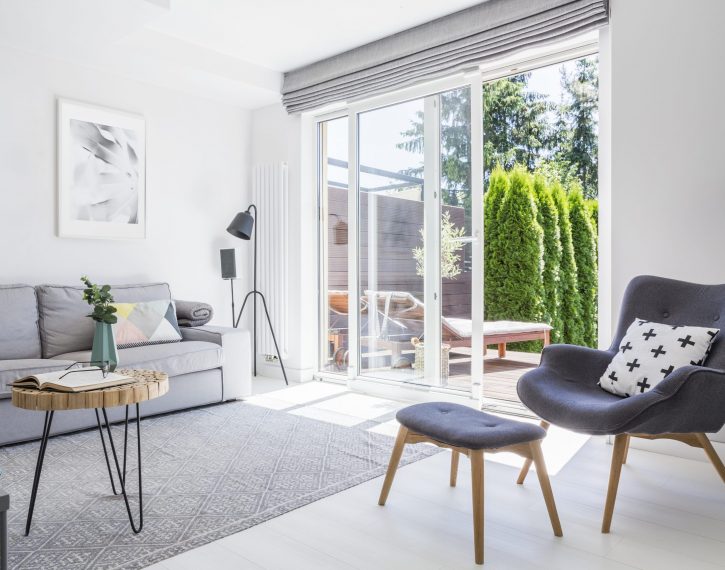 Armchair with patterned pillow and stool in living room interior with grey sofa and posters. Real photo